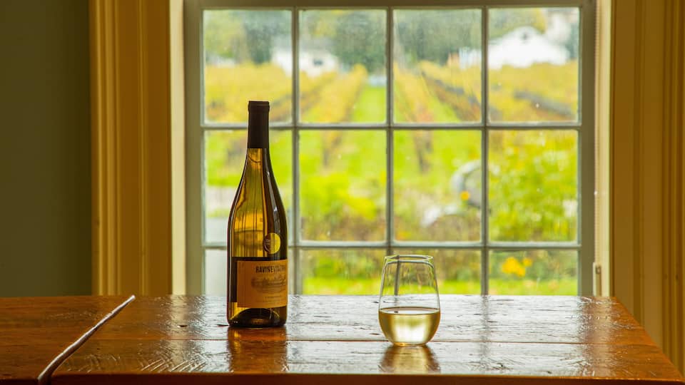 A bottle of Ravine Vineyard Chardonnay and a glass on a wooden table by a window with a vineyard view.