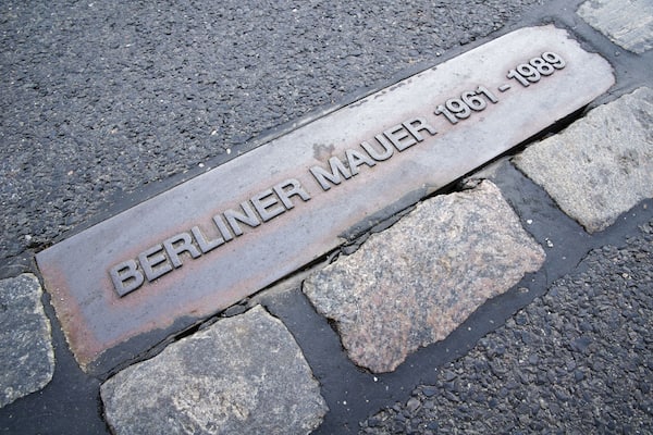 Une plaque métallique portant l’inscription « BERLINER MAUER 1961-1989 » est fixée sur un pavé.