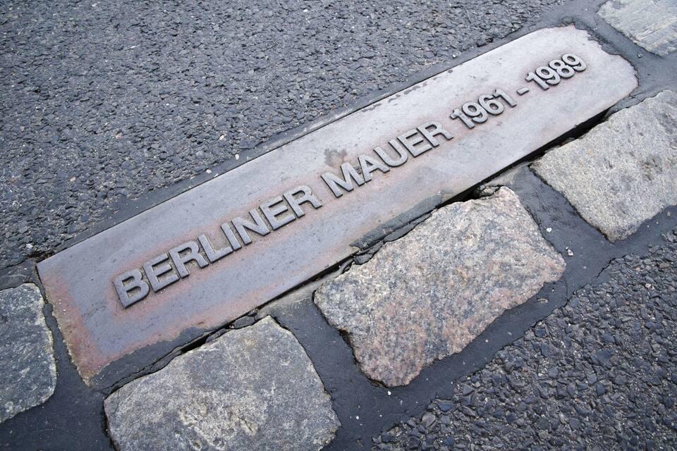 A metal plaque with the inscription "BERLINER MAUER 1961-1989" on a cobblestone pavement.