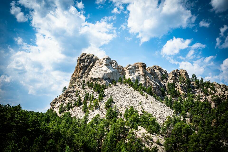 A mountain with prominent rock formations and a forested base.