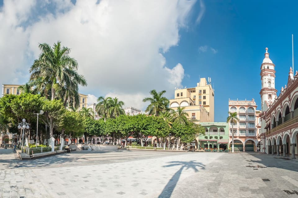 A historic plaza with colonial architecture, palm trees, and a prominent church tower.