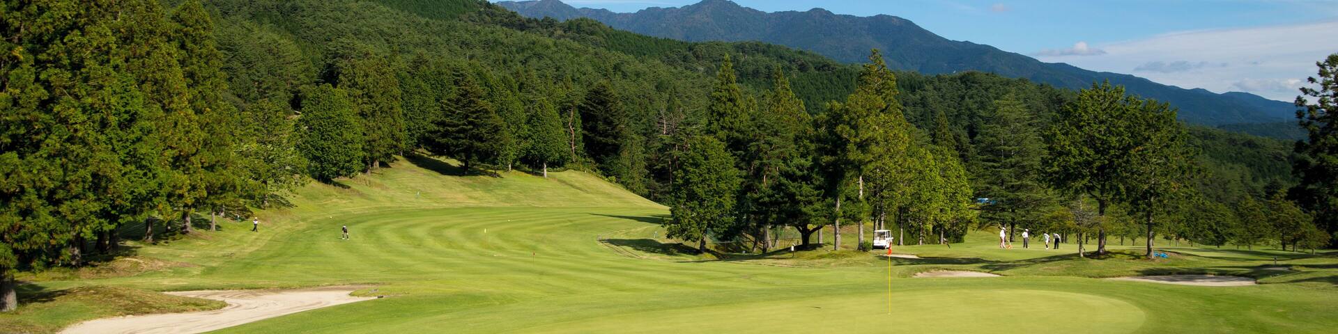 A golf course with a mountainous backdrop and dense forest.