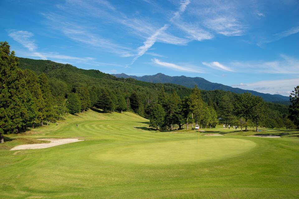 A golf course with a mountainous backdrop and dense forest.