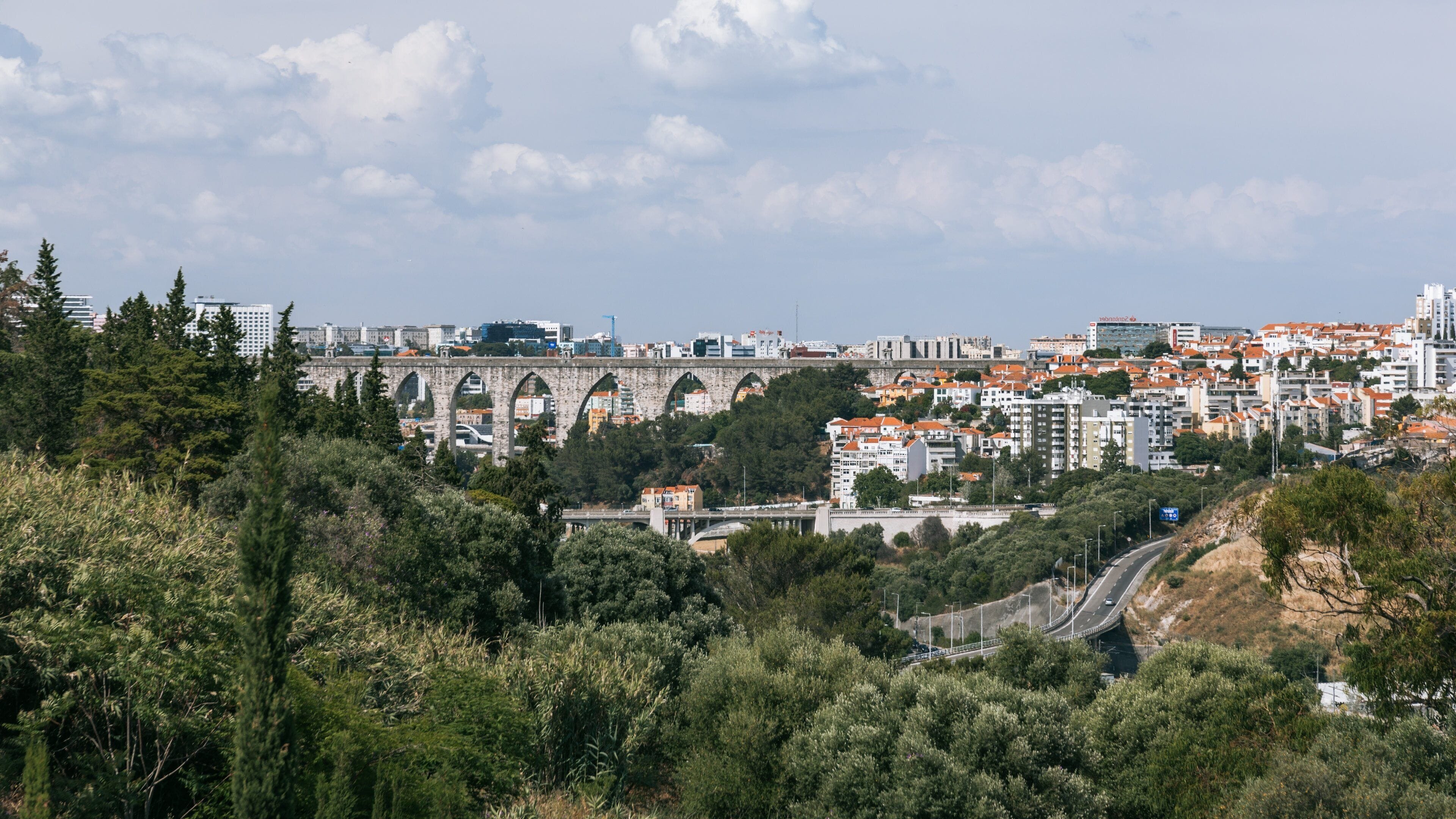 A cityscape with a prominent stone bridge, dense greenery, and a mix of residential and commercial buildings.