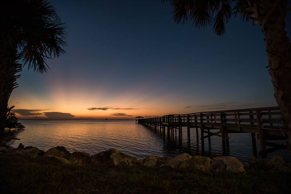 A sunset over a calm body of water with a wooden pier extending into the water.
