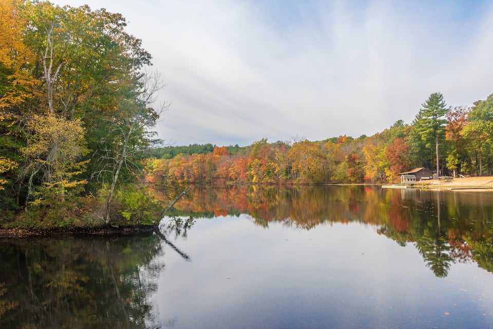 A calm lake surrounded by autumn-colored trees and a small dock.