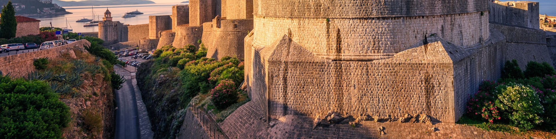 A historic stone fortress with a round tower, a fortified wall, and a coastal backdrop.