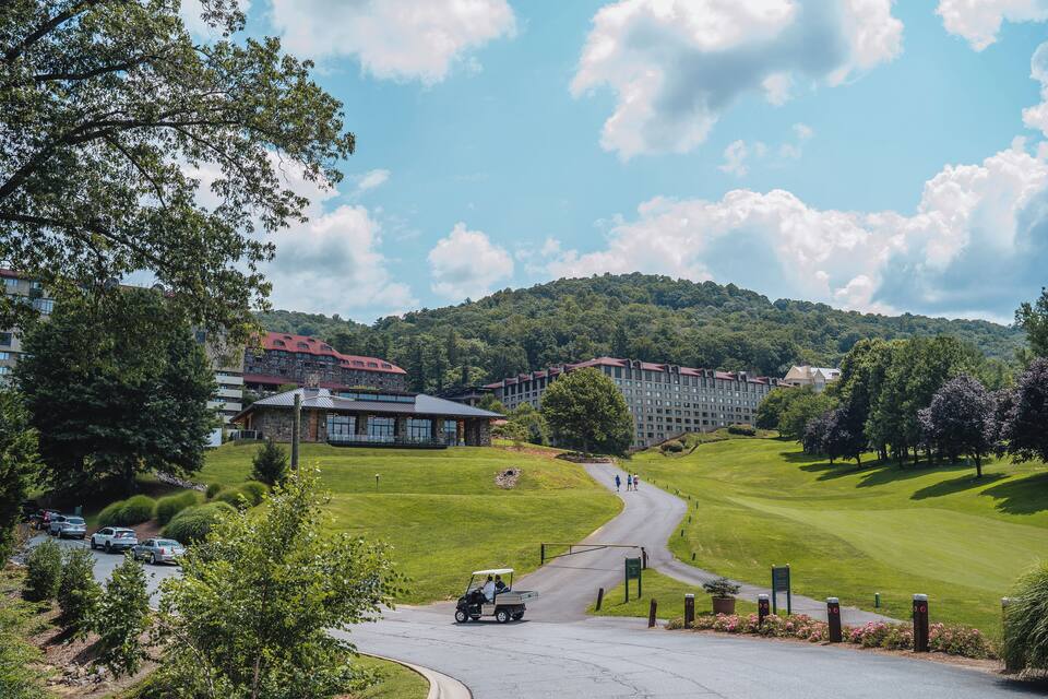 Um campo de golfe com um clube, um estacionamento e uma paisagem arborizada com colinas.