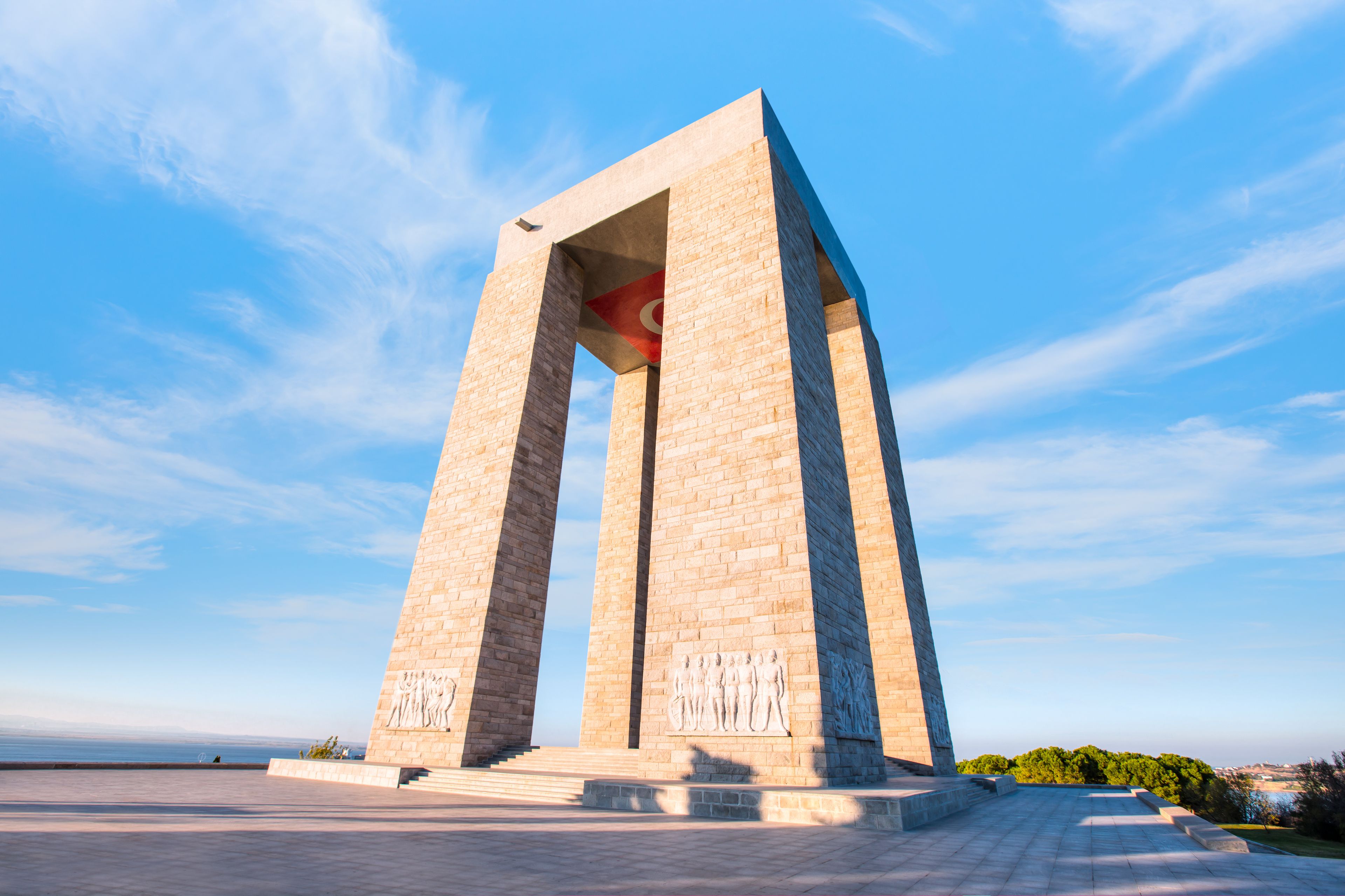 A large stone monument with a flag on top, set against a clear blue sky.