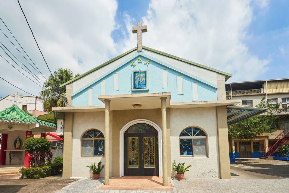 Eine Kirche mit blauer Fassade, einem Kreuz und einem religiösen Gemälde über dem Eingang.