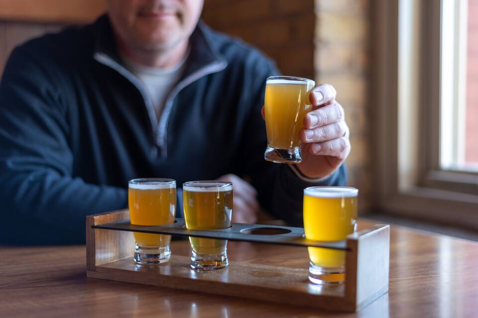 A person holding a glass of beer with four other glasses on a tray.