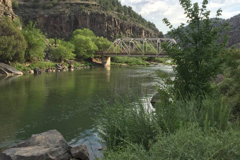 A river with a bridge, rocky cliffs, and green vegetation.