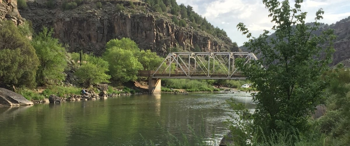 A river with a bridge, rocky cliffs, and green vegetation.