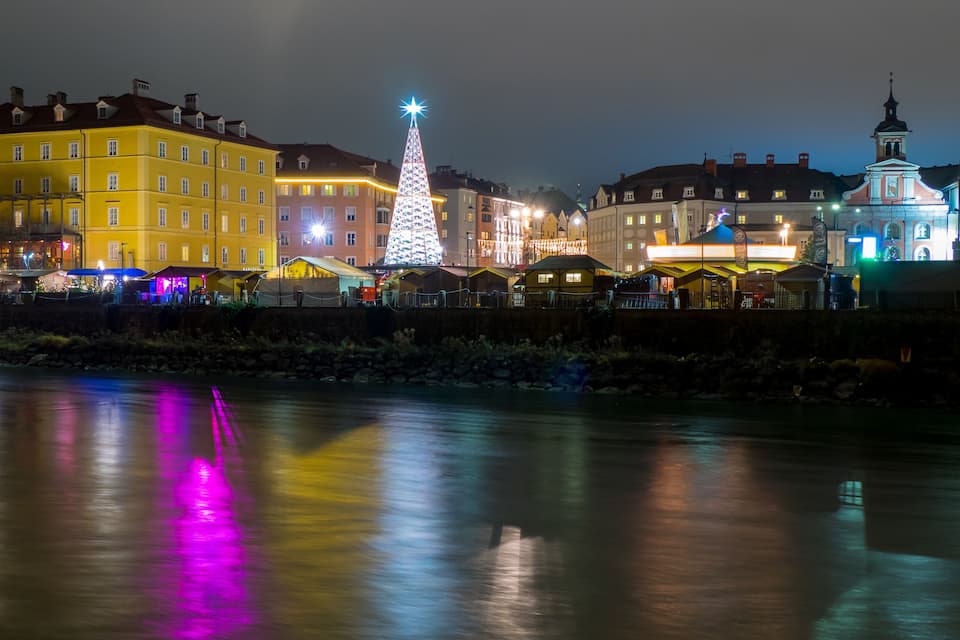 A river reflecting colorful lights from buildings and a Christmas tree.