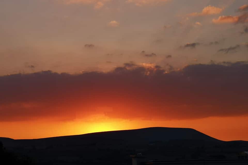 Un coucher de soleil sur un paysage vallonné, avec un bâtiment au premier plan.