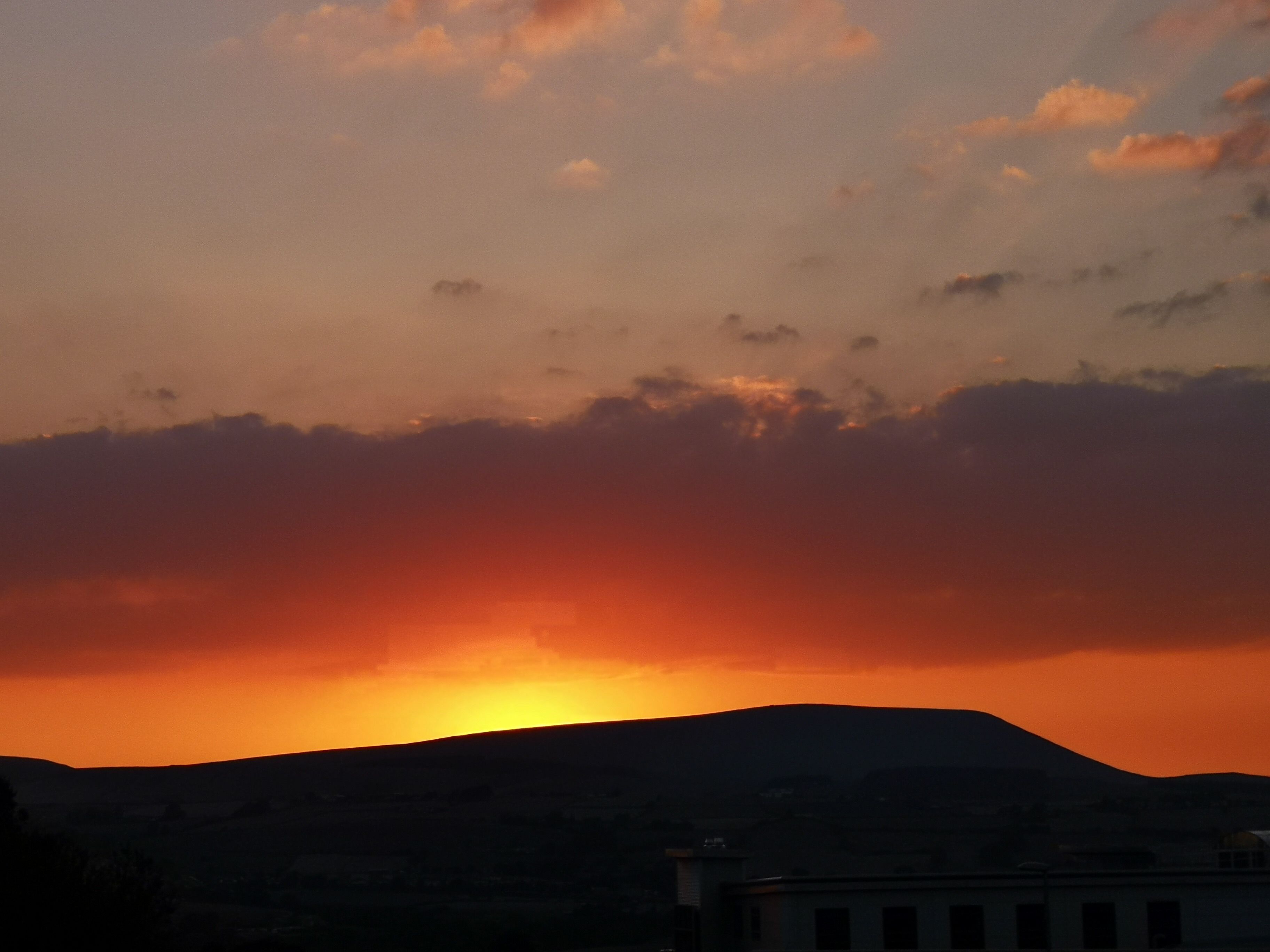 A sunset over a hilly landscape with a building in the foreground.