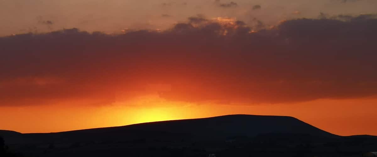 A sunset over a hilly landscape with a building in the foreground.