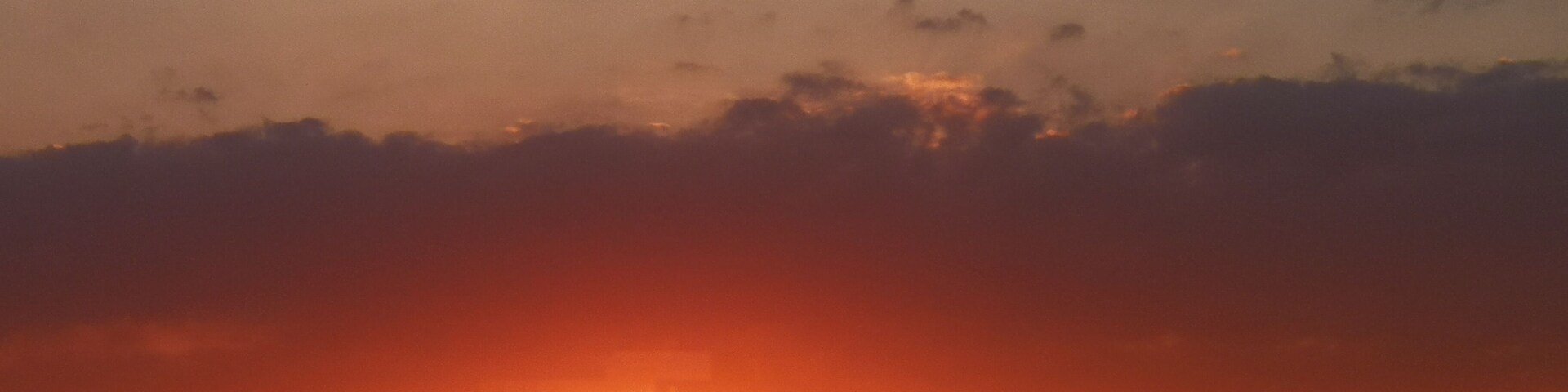 A sunset over a hilly landscape with a building in the foreground.