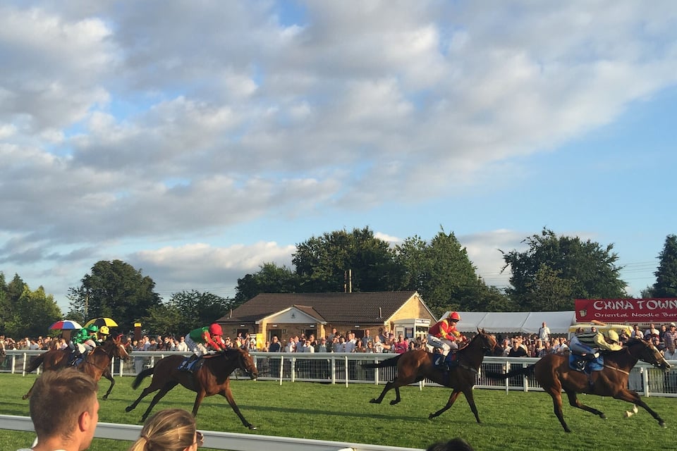 Une course de chevaux avec des jockeys à cheval, des spectateurs et une pancarte indiquant l’entrée de Chinatown.
