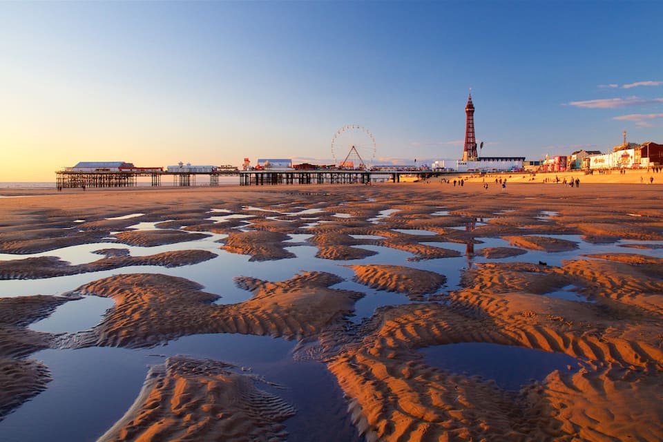 A beach with a pier, a Ferris wheel, and a tall tower.
