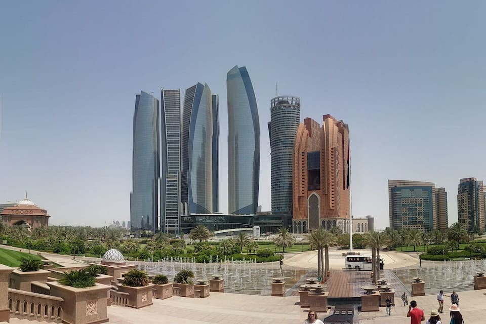 A cityscape with modern skyscrapers, a central fountain, and landscaped gardens.