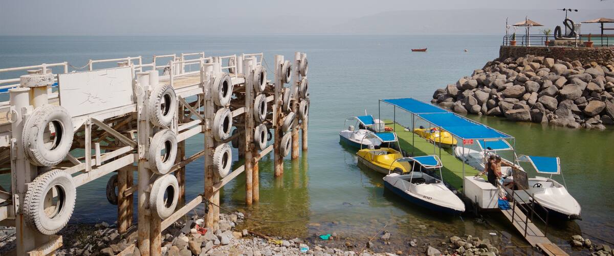 A pier with a unique tire barrier, boats docked, and a rocky shoreline.