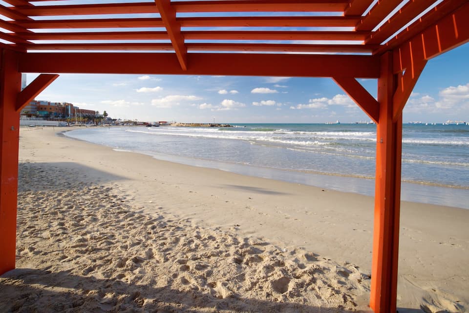 Une plage avec une structure en bois rouge, un rivage sablonneux et des vagues de l’océan.