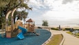 Un parque infantil con un tobogán azul y una casita de madera junto a la playa.