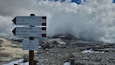 Ein Wegweiser am Bergpfad mit Zielorten und Entfernungen.