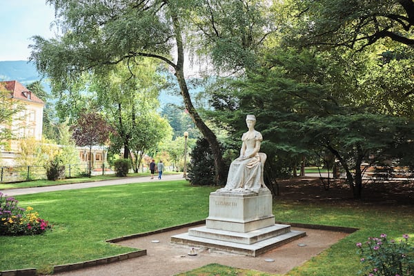 Une statue d’une femme nommée Élisabeth, dans un parc avec des arbres et un bâtiment en arrière-plan.
