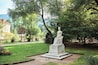 A statue of a woman named Elisabeth in a park with trees and a building in the background.