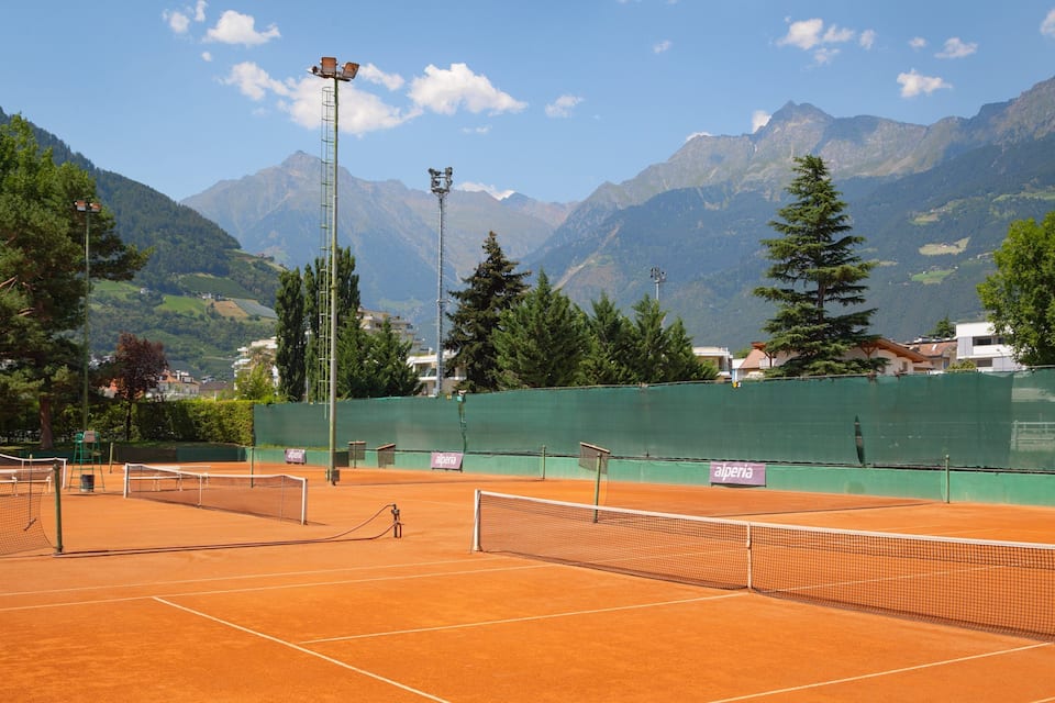 A tennis court with netted areas, surrounded by mountains and trees.