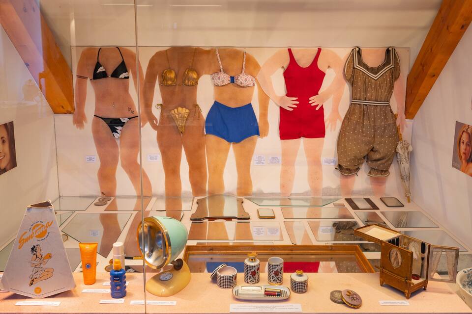 A museum exhibit with mannequins in vintage swimwear, vintage cosmetics, and a vintage radio.