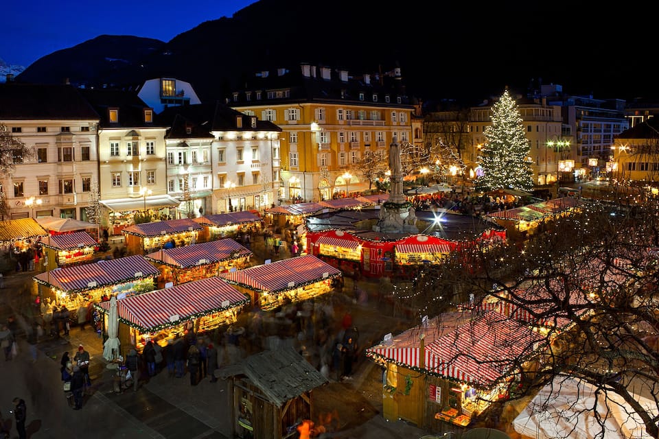 A bustling market square at night with illuminated stalls and a large Christmas tree.