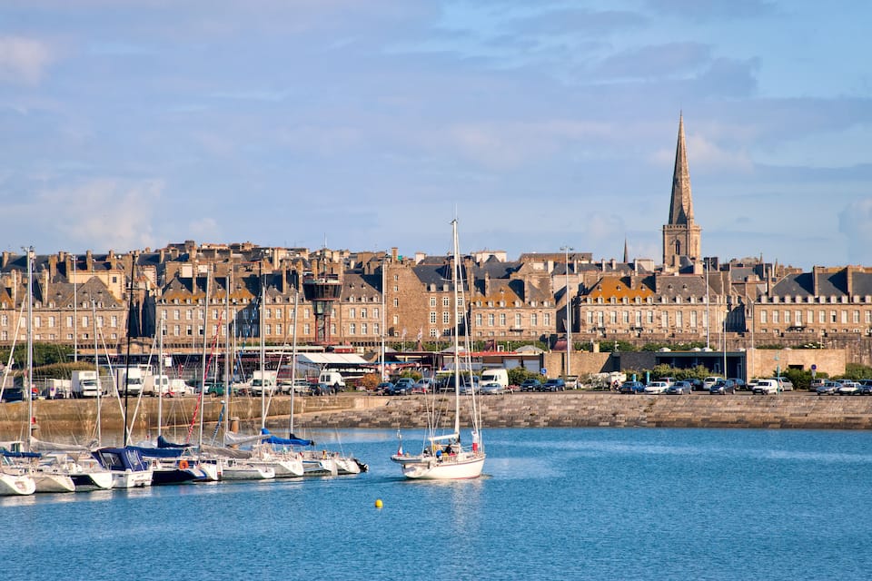A harbor with boats and a prominent church spire in the background.