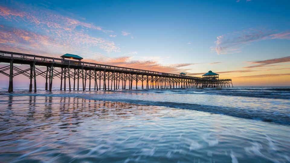A pier extending into the ocean with a sunset in the background.