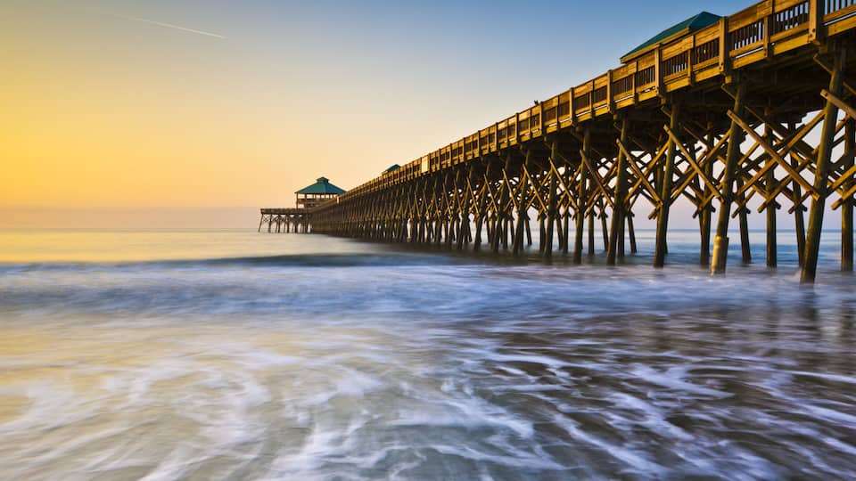 A wooden pier extending into calm waters at sunset.