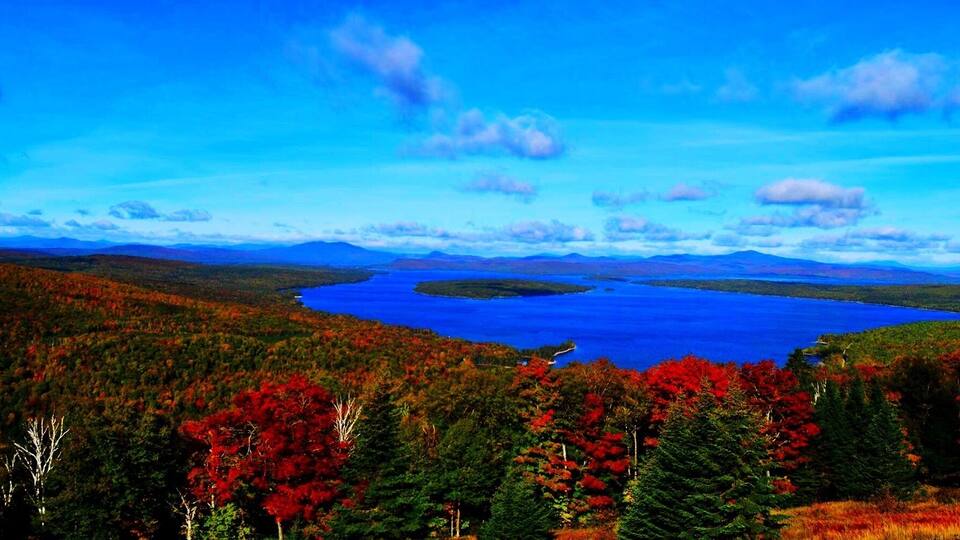 A lake surrounded by autumn-colored forests and distant mountains under a clear sky.
