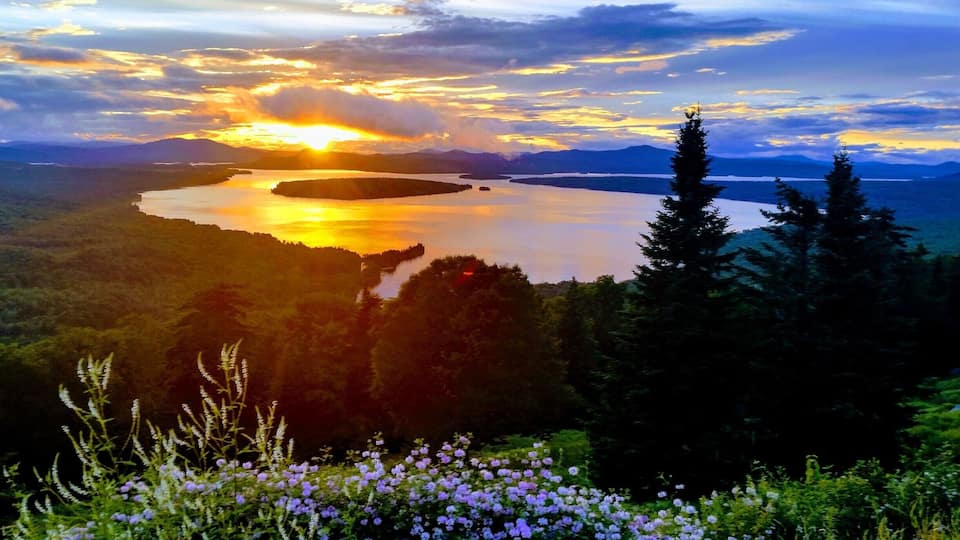 A sunset over a lake surrounded by forested hills.