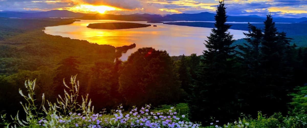 A sunset over a lake surrounded by forested hills.