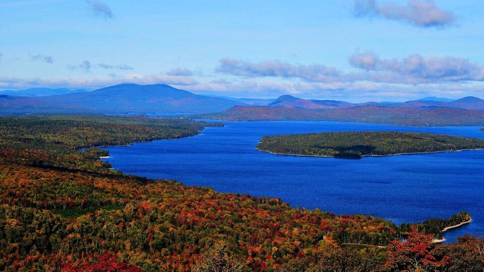 A lake surrounded by autumn-colored forests and distant mountains.