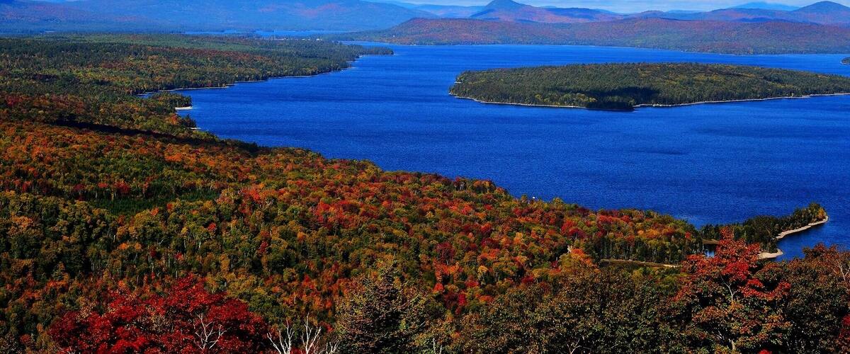 A lake surrounded by autumn-colored forests and distant mountains.