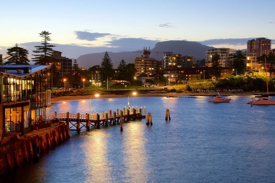 A waterfront cityscape at dusk with buildings, a dock, and boats.