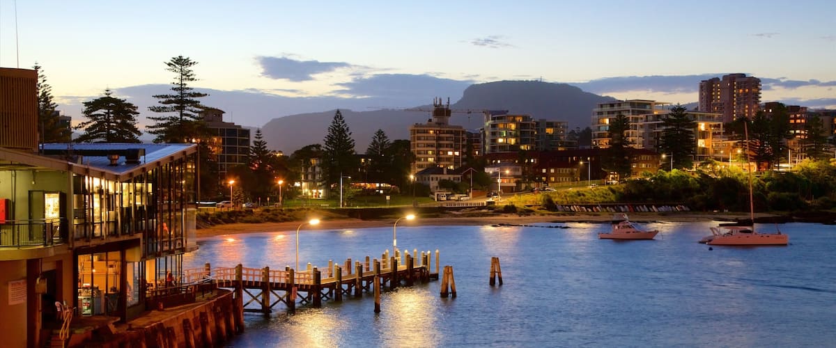 A waterfront cityscape at dusk with buildings, a dock, and boats.