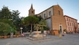 A historic square with a church tower, a fountain, and a statue.