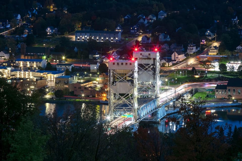 Un pont sobre un riu, envoltat d'edificis residencials i una torre il·luminada.
