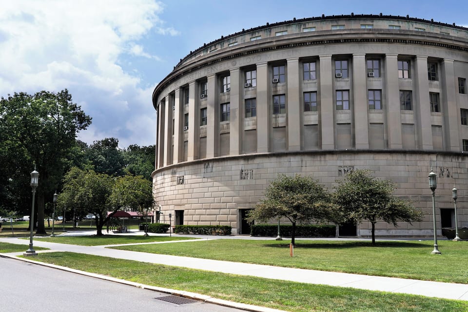 A large, circular building with columns and a dome, surrounded by a well-maintained lawn and trees.