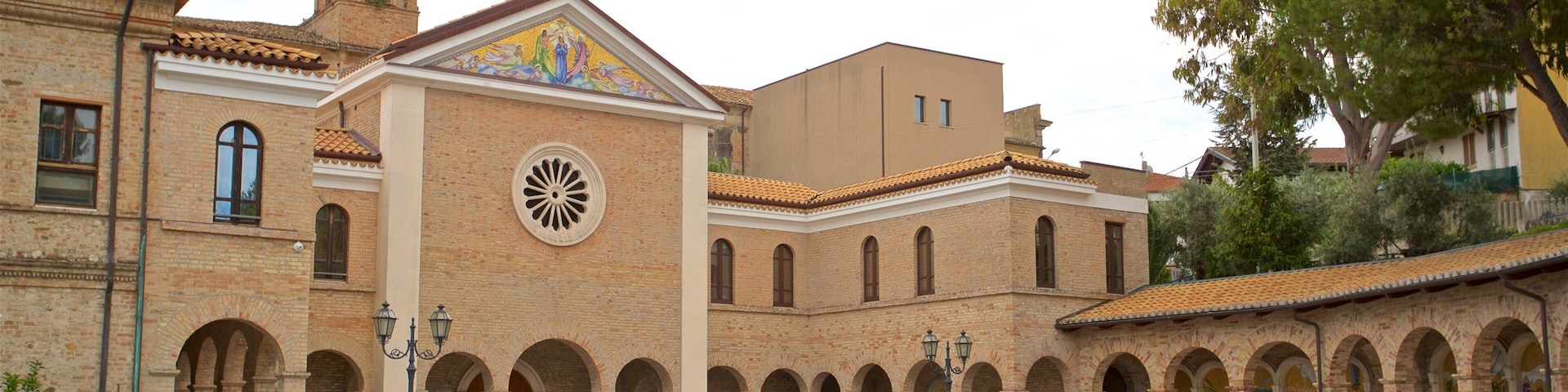 Uma igreja histórica com uma torre de sino, varandas em arco e uma van branca estacionada em frente.