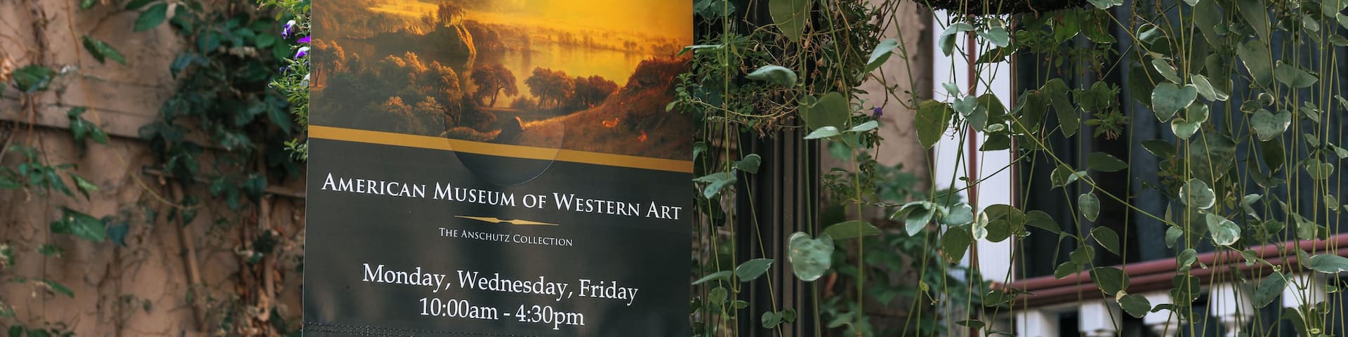 Un cartel de museo con una pintura de paisaje, colgado de un edificio cubierto de hiedra.