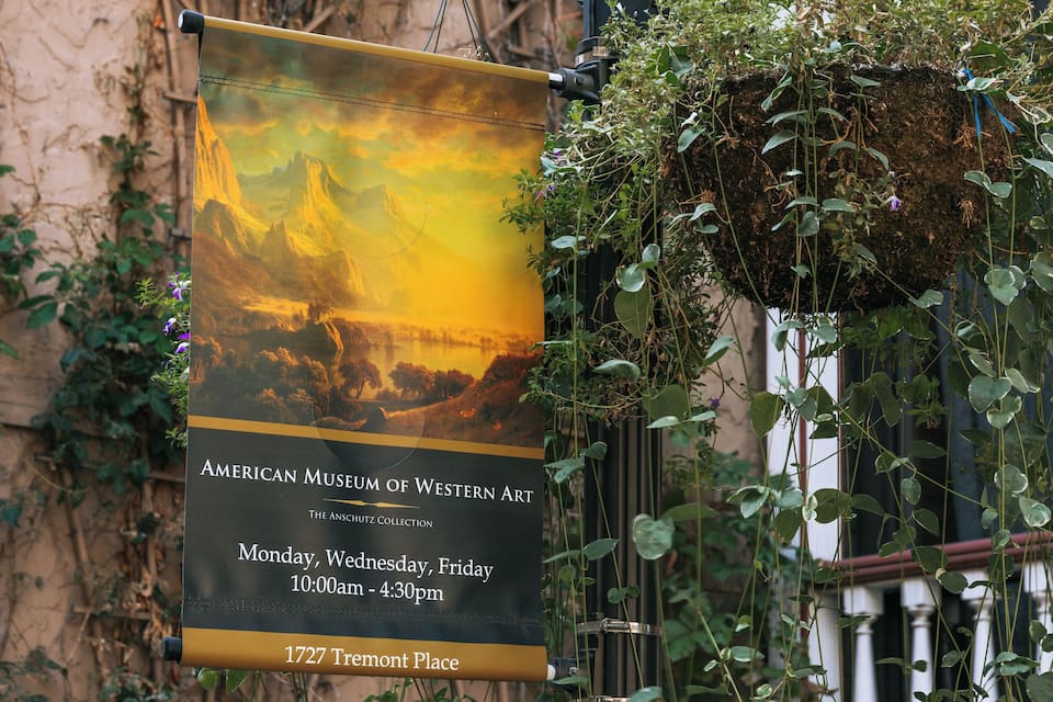 A museum banner with a landscape painting, hanging from a building with ivy.